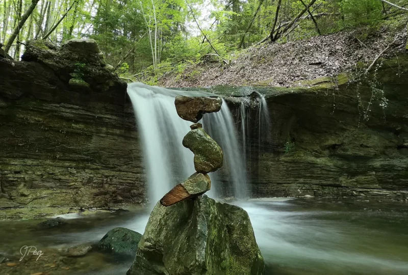 Balanced rocks by serene waterfall in forest.
