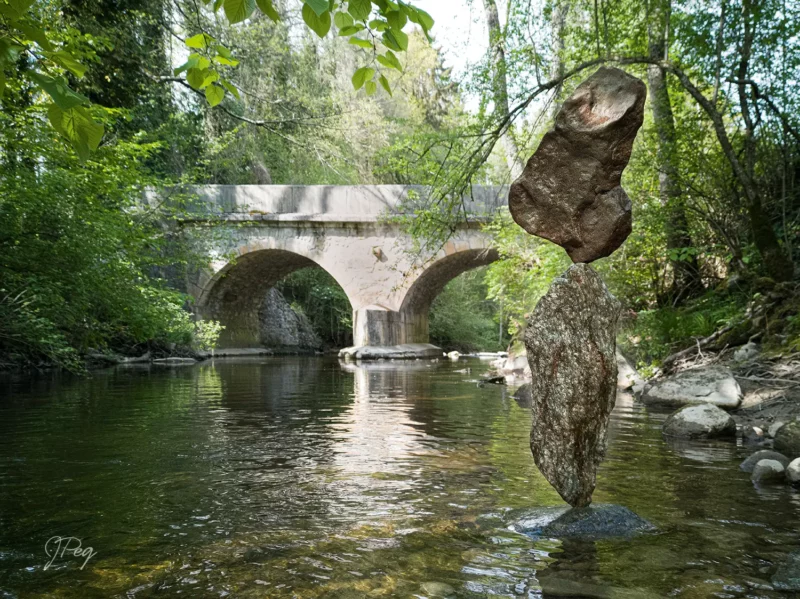 Rock balance in forest stream near stone bridge.