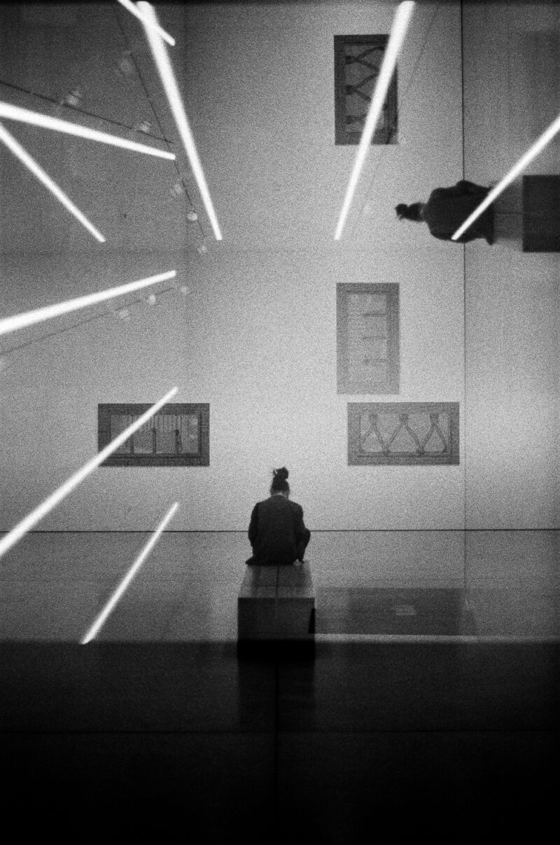 Person in gallery viewing abstract artwork, blurred reflections.