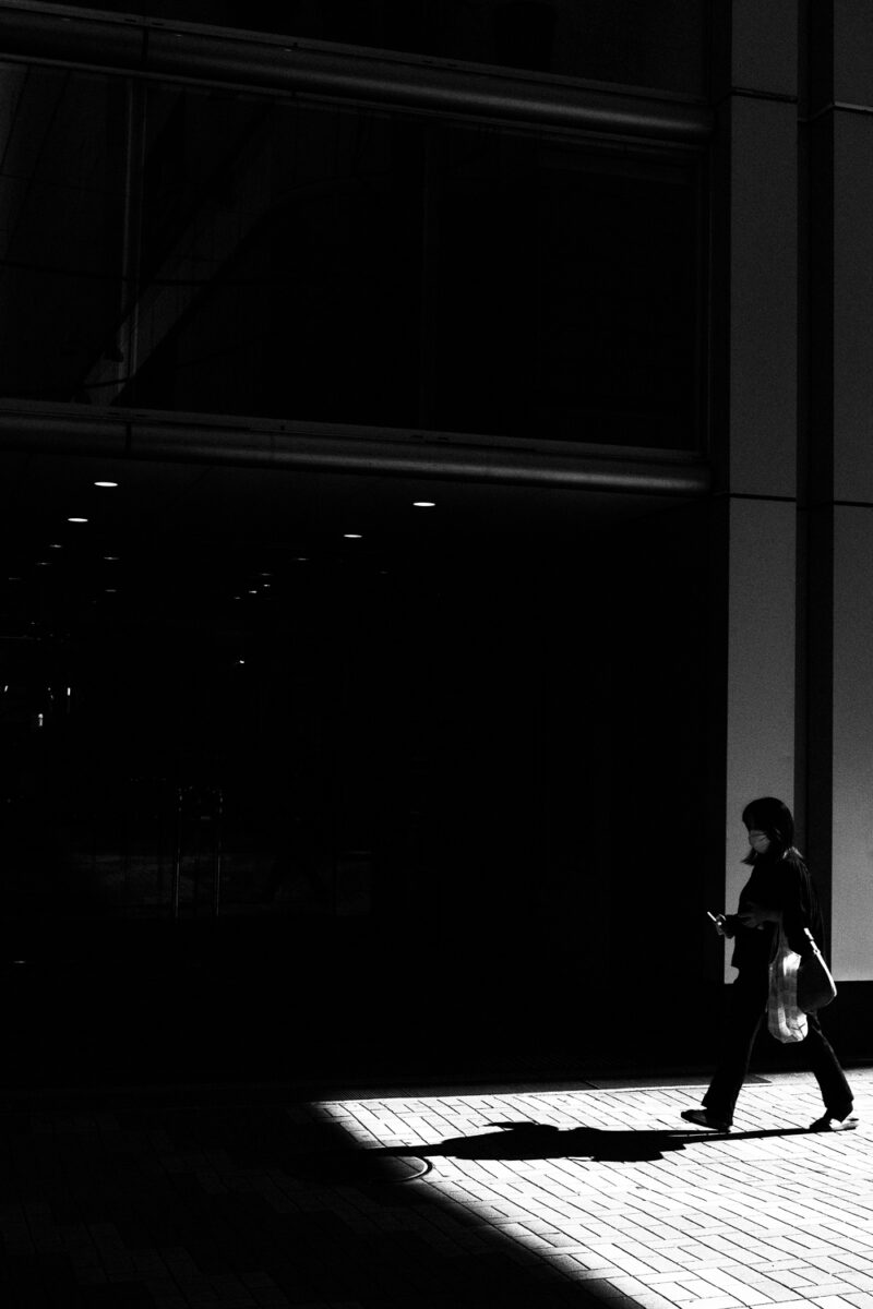 Persona di profilo che cammina alla luce del sole con il cellulare