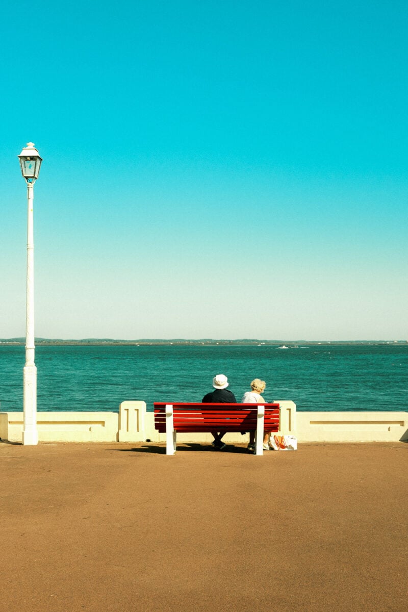 Couple sitting on a seaside bench under lamp post.