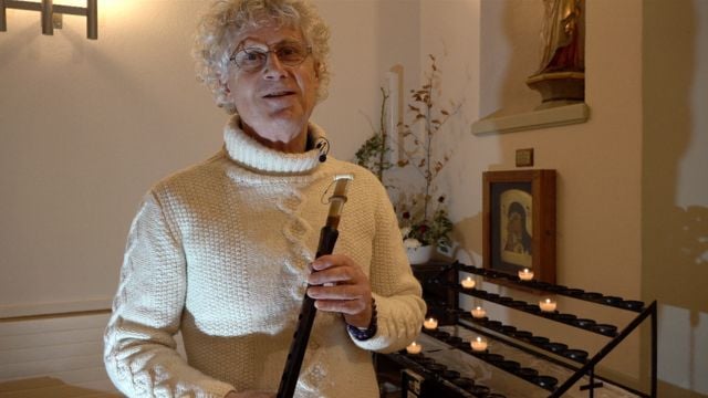 Persona con bastone da passeggio all'interno di una cappella illuminata da candele