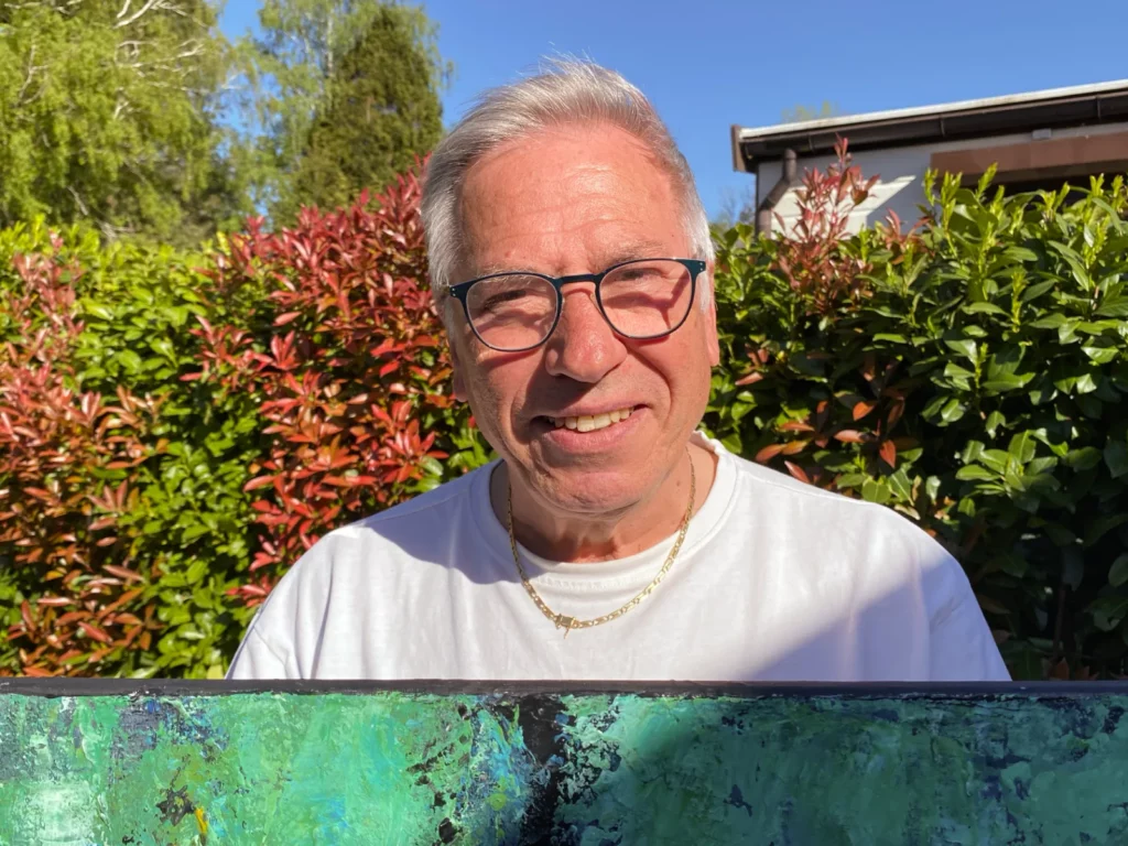 Smiling man holding abstract painting in sunny garden