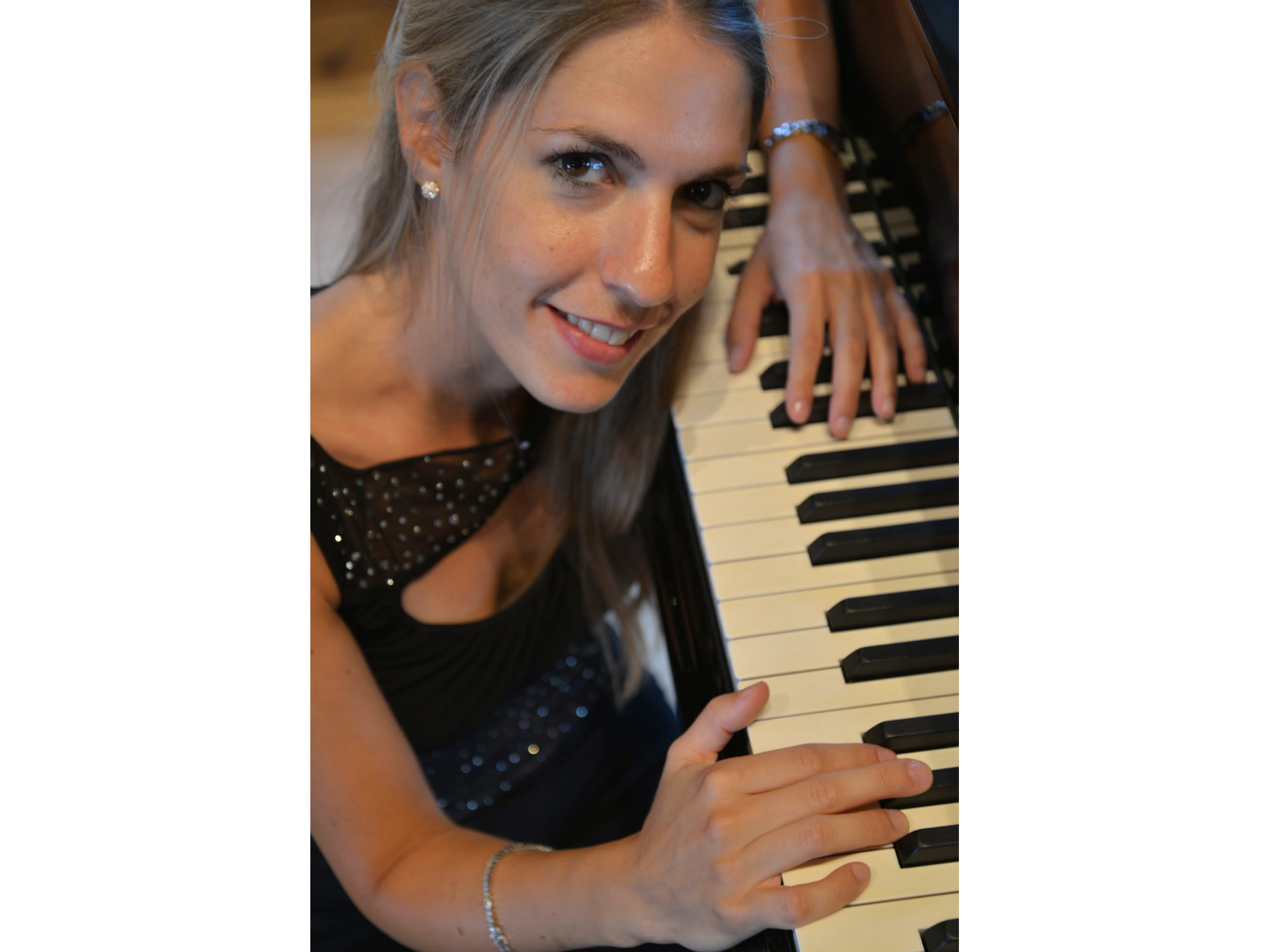 Une femme souriante qui joue du piano et regarde l'appareil photo